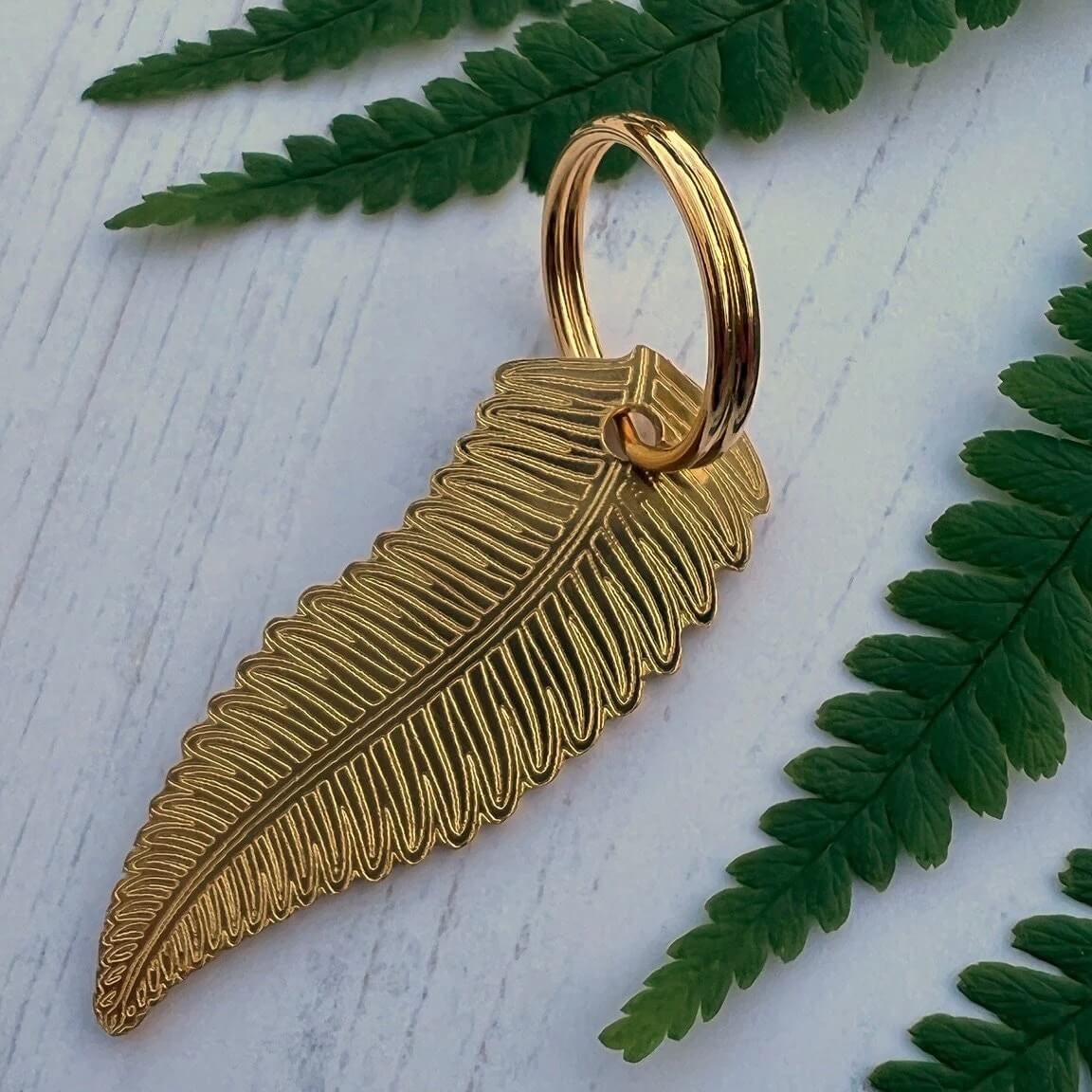 Gold fern leaf tag on a white surface with green leaves