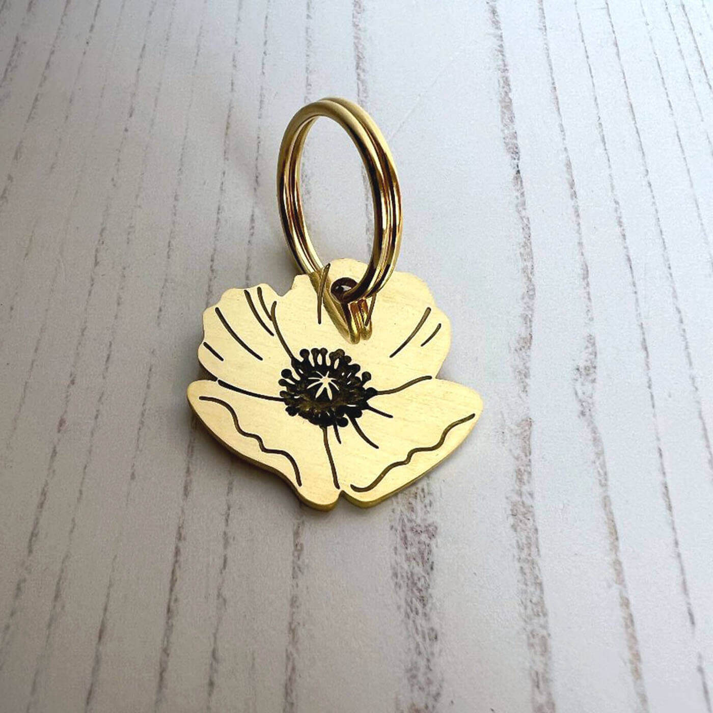 Brass flower-shaped dog name tag on a light wooden surface