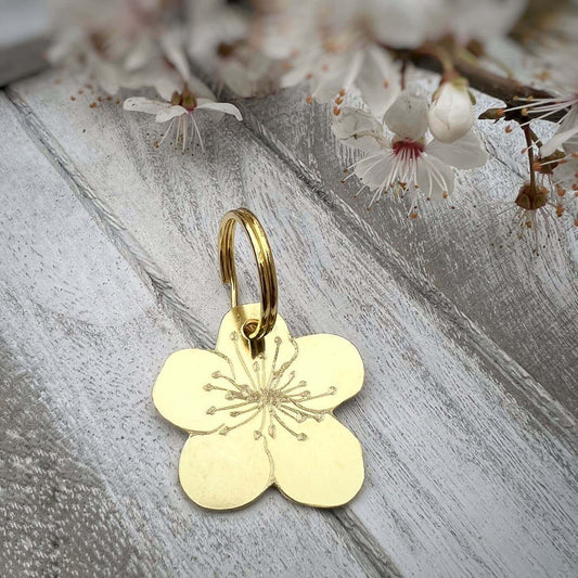 Gold flower tag on a wooden surface with cherry blossoms in the background