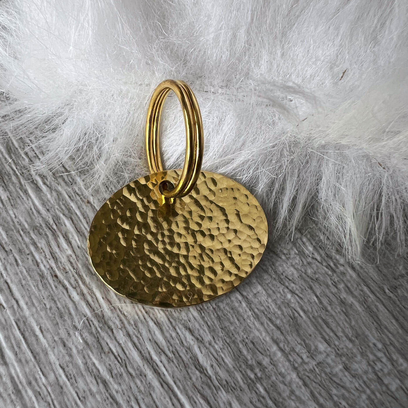 Gold textured pendant on a wooden surface with white fur background