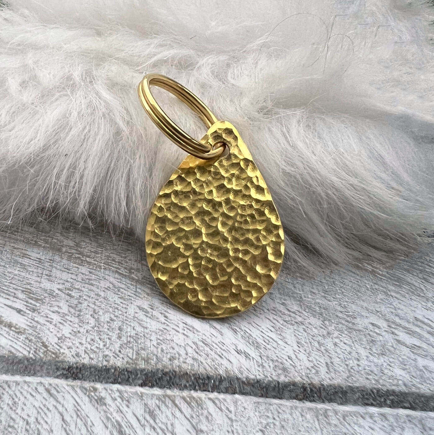 Brass teardrop-shaped dog ID tag on a white fur background