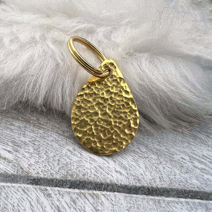 Brass teardrop-shaped dog ID tag on a white fur background