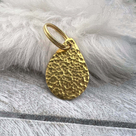 Brass teardrop-shaped dog ID tag on a white fur background