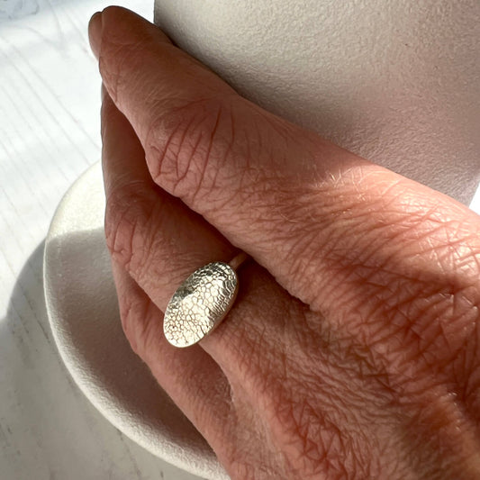 Hand wearing a nose print textured silver ring on a neutral background