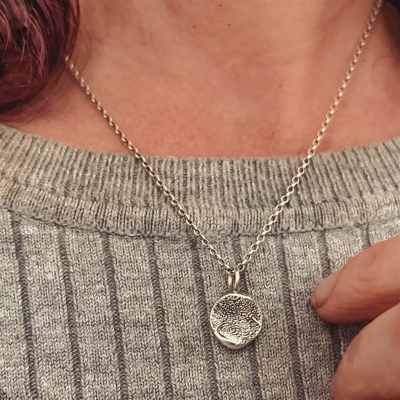 Silver necklace with a round paw print pendant worn by a person in a gray sweater.