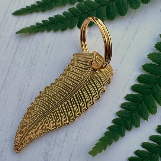 Gold fern leaf tag on a white surface with green leaves