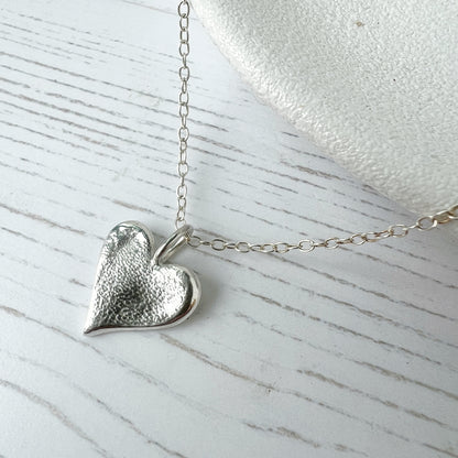 Silver heart-shaped textured pendant on a chain against a light background