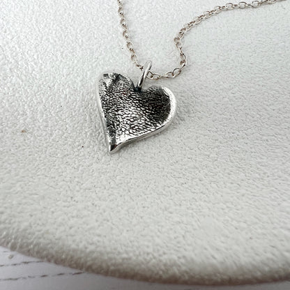 Silver blackened textured heart-shaped pendant on a chain against a white background