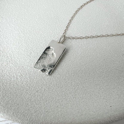 Silver pendant necklace with imprint texture on a light gray background