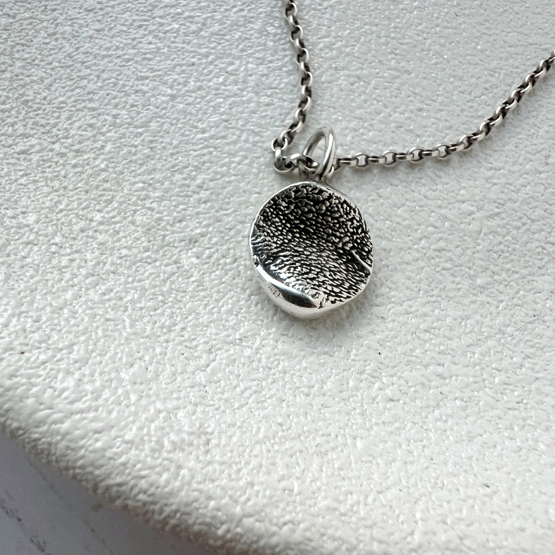 Silver textured organic pendant necklace on a  white surface