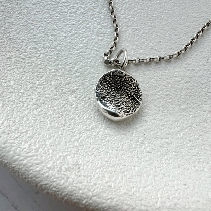 Silver textured organic pendant necklace on a  white surface