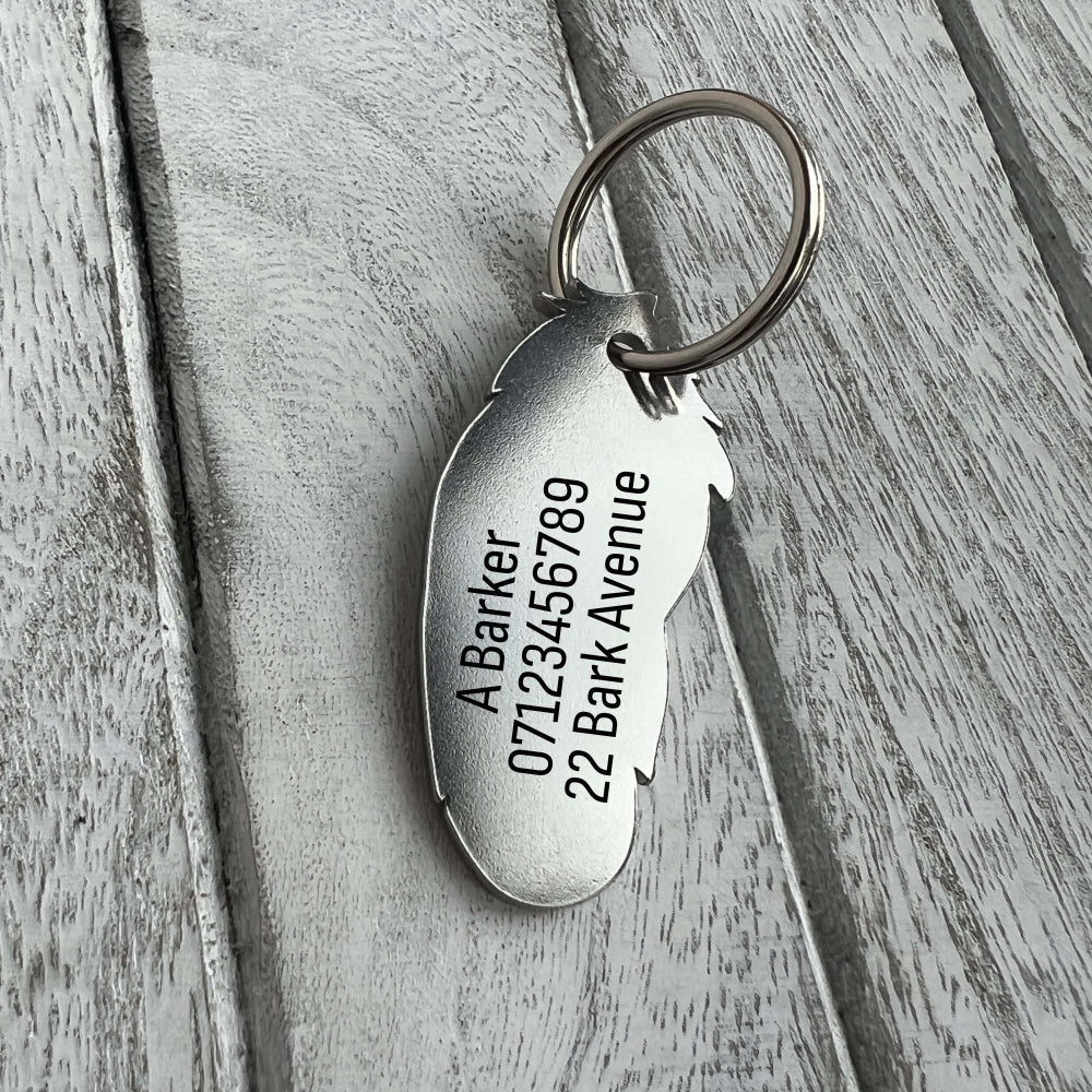 Silver coloured stainless steel feather shaped pet ID tag on wooden background