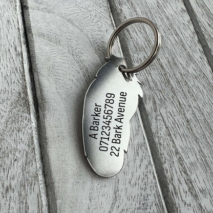 Silver coloured stainless steel feather shaped pet ID tag on wooden background